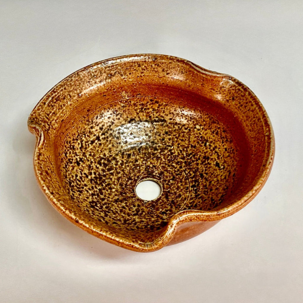 Handcrafted amber stoneware planter with speckled glaze and drainage hole viewed from above.