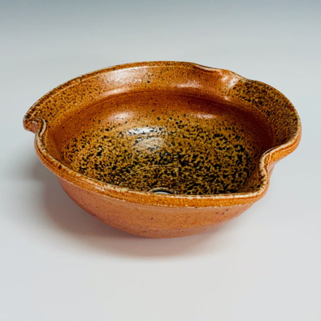 Side view of handmade amber stoneware planter showing organic wavy rim and textured exterior.