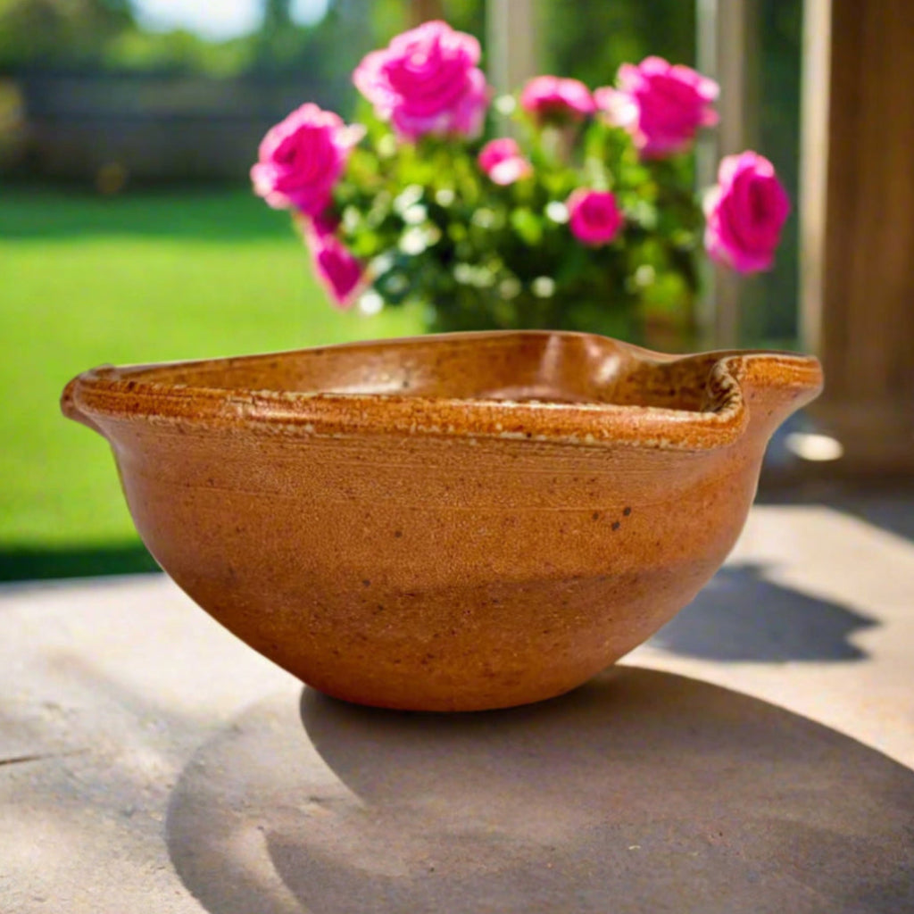 artisan amber stoneware planter sitting on a patio with pink roses and green grass in the background.
