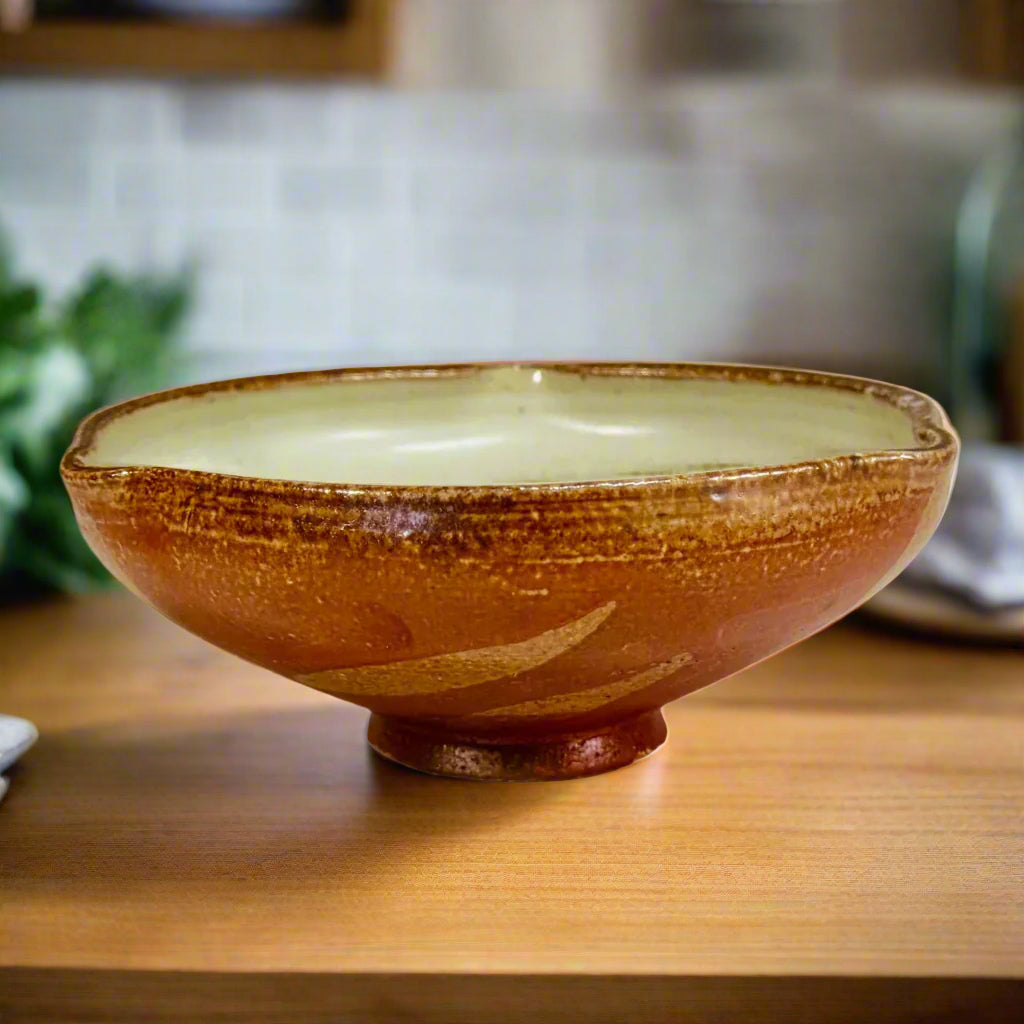 Handcrafted wood-fired ceramic bowl with amber-brown exterior, cream interior, and flowing decorative pattern, made in Danbury, NC.