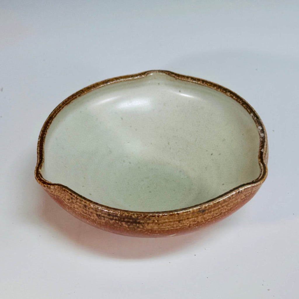 Handcrafted wood-fired ceramic bowl with amber-brown exterior, cream interior, and flowing decorative pattern, made in Danbury, NC.