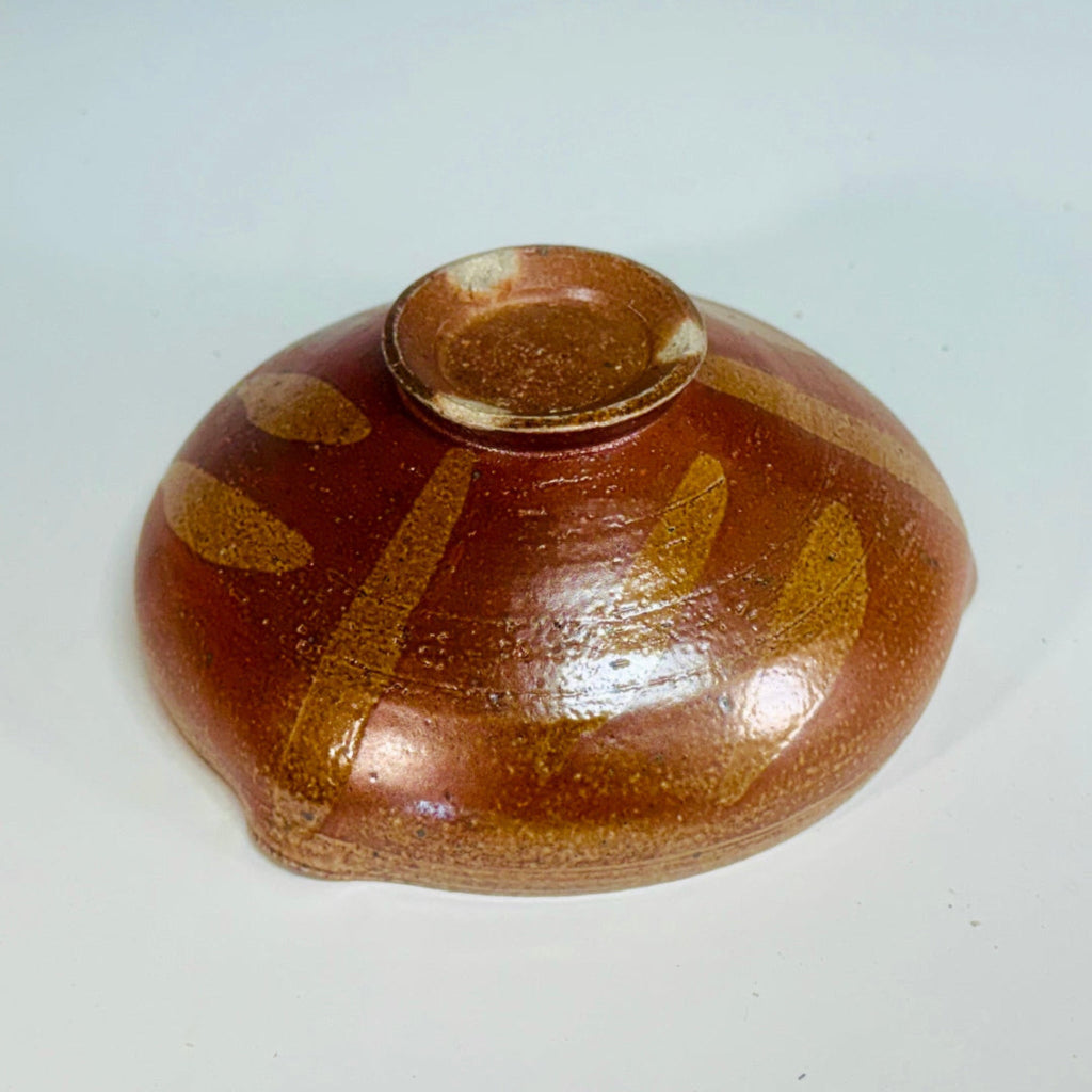 Handcrafted wood-fired ceramic bowl with amber-brown exterior, cream interior, and flowing decorative pattern, made in Danbury, NC.