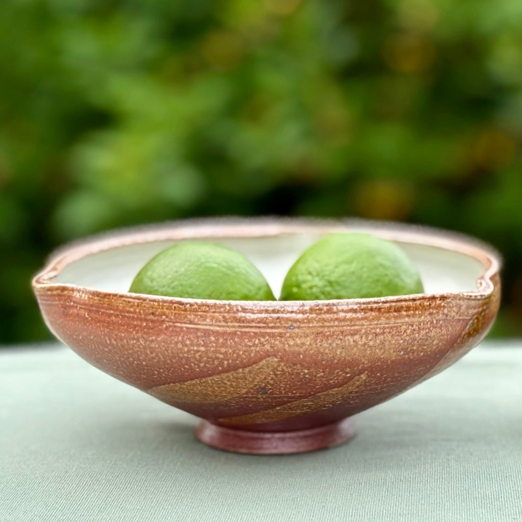 with amber-brown exterior, cream interior, and flowing decorative pattern with two limes inside the bowl, made in Danbury, NC. 