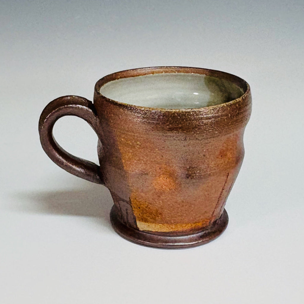 Handcrafted wood-fired brown stoneware mug with white interior and curved handle from Danbury pottery.
