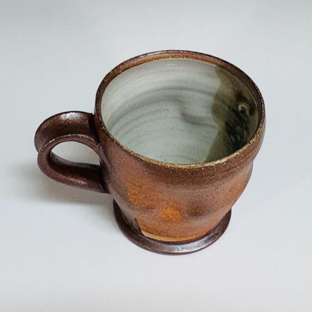 Handcrafted wood-fired brown stoneware mug with white interior and curved handle from Danbury pottery.