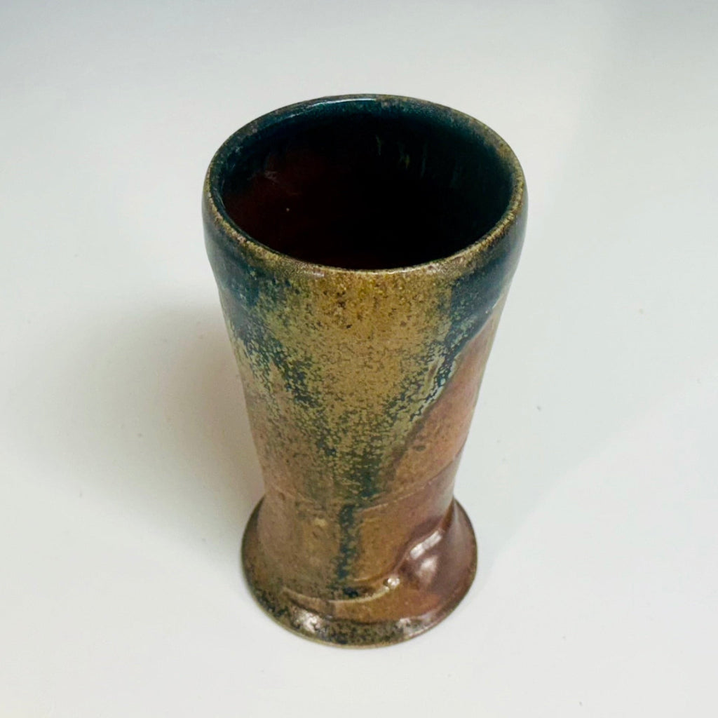 Handcrafted wood-fired ceramic tumbler with amber and natural clay accents, top/side view showing glaze patterns.