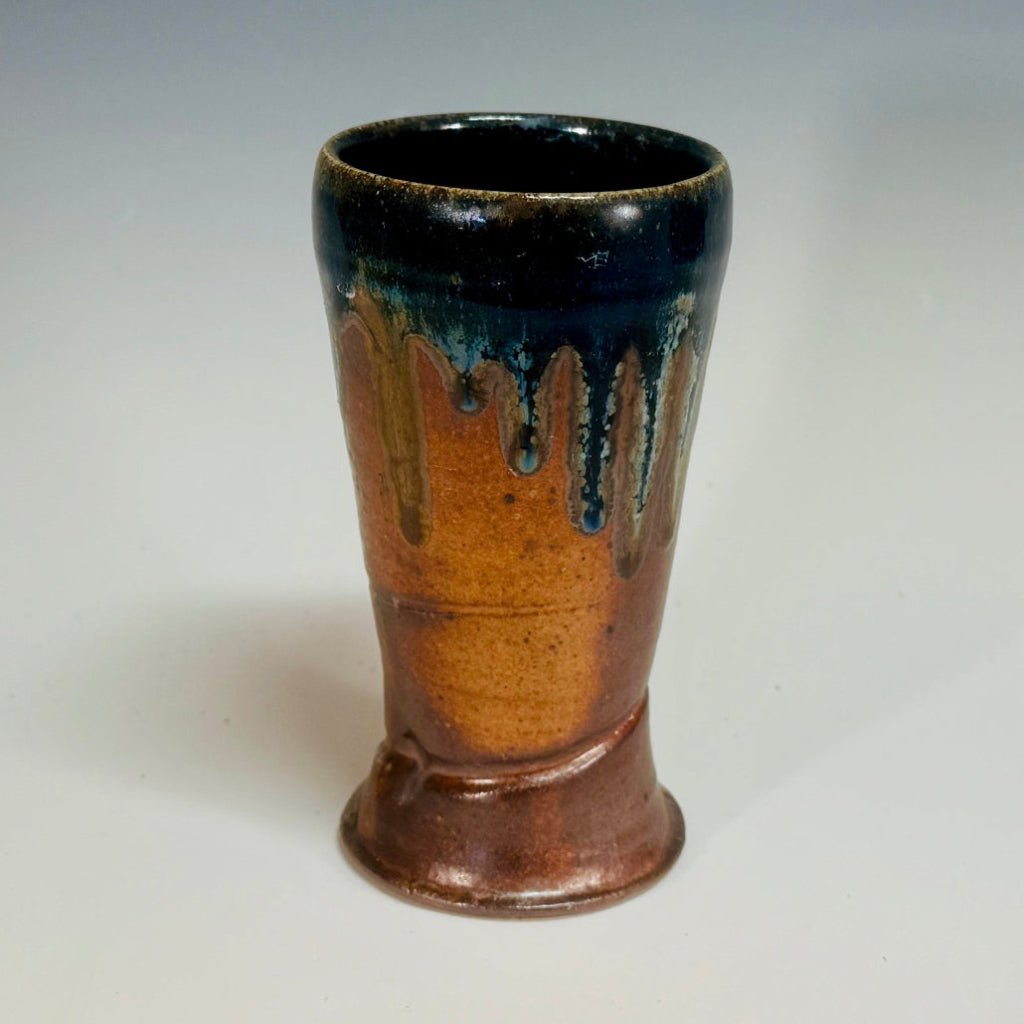 Handcrafted wood-fired ceramic tumbler with amber and natural clay accents with cobalt drips, side view showing glaze patterns.