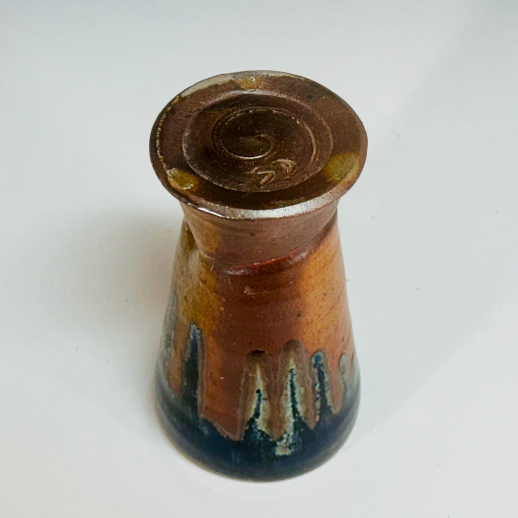 Handcrafted wood-fired ceramic tumbler with amber and natural clay accents, bottom view showing glaze patterns.