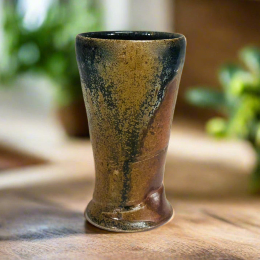 Handcrafted wood-fired ceramic tumbler with amber and natural clay accents on a countertop.