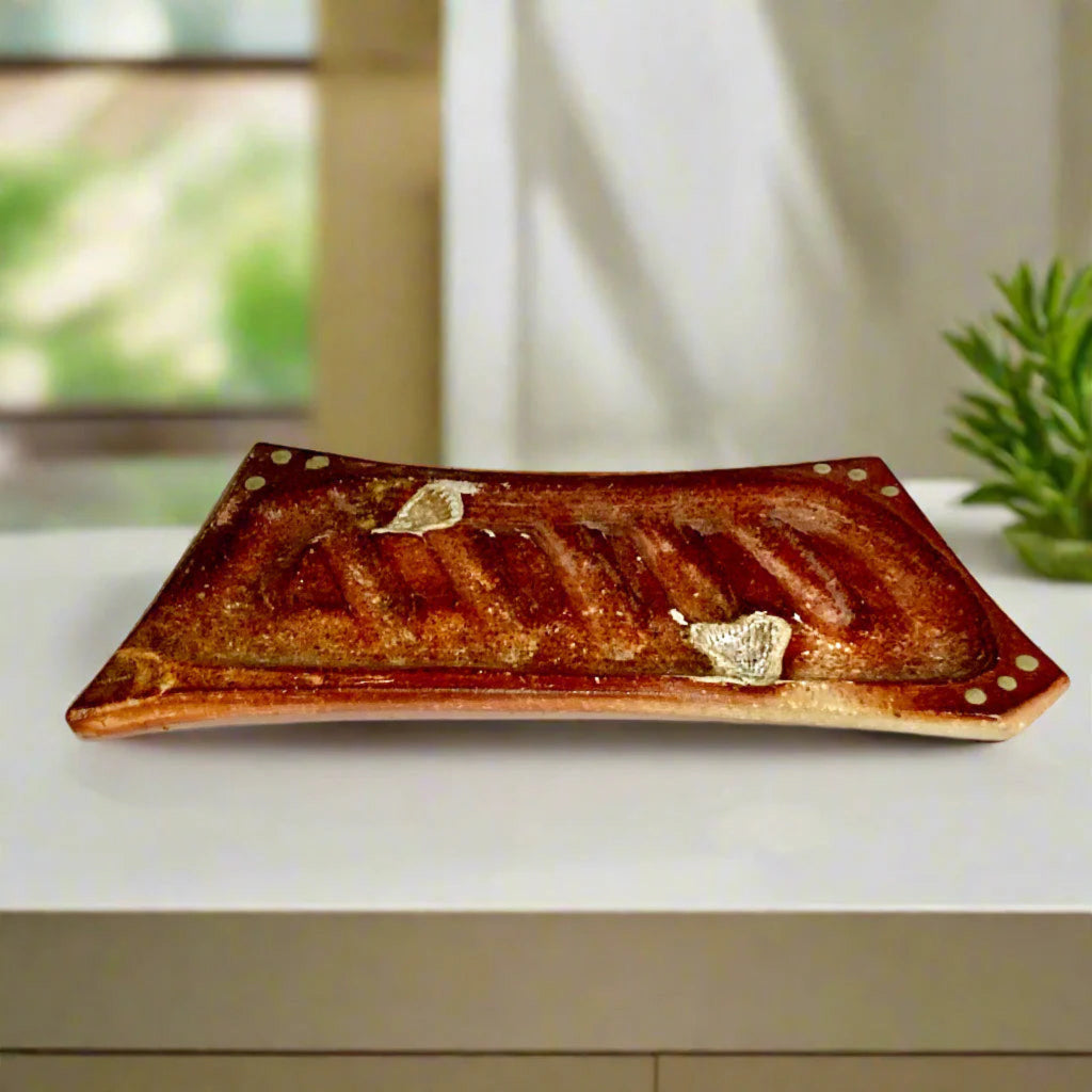 Handmade rectangular soap dish with ridged design and decorative dots in rustic terracotta tones on a countertop.