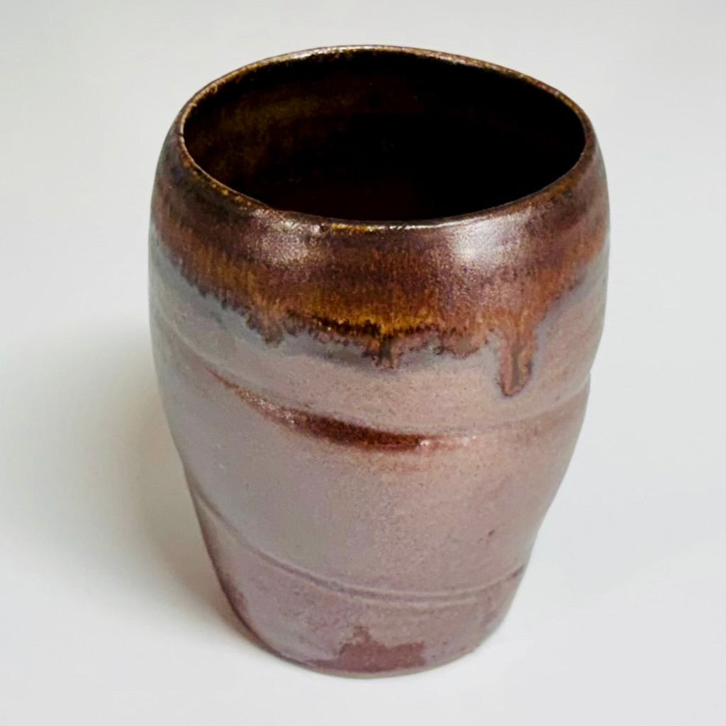 Handcrafted wood-fired ceramic tumbler with mauve-brown body and flowing amber glaze detail, made in Danbury, NC.