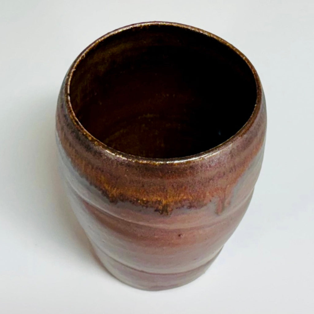 Top view: Handcrafted wood-fired ceramic tumbler with mauve-brown body and flowing amber glaze detail, made in Danbury, NC.