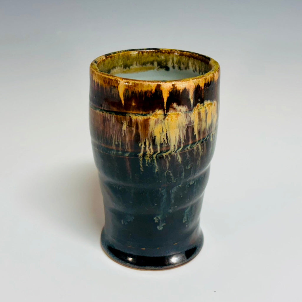 Handcrafted stoneware tumbler with horizontal ridges and blue-black to amber wood-fired glaze effect.