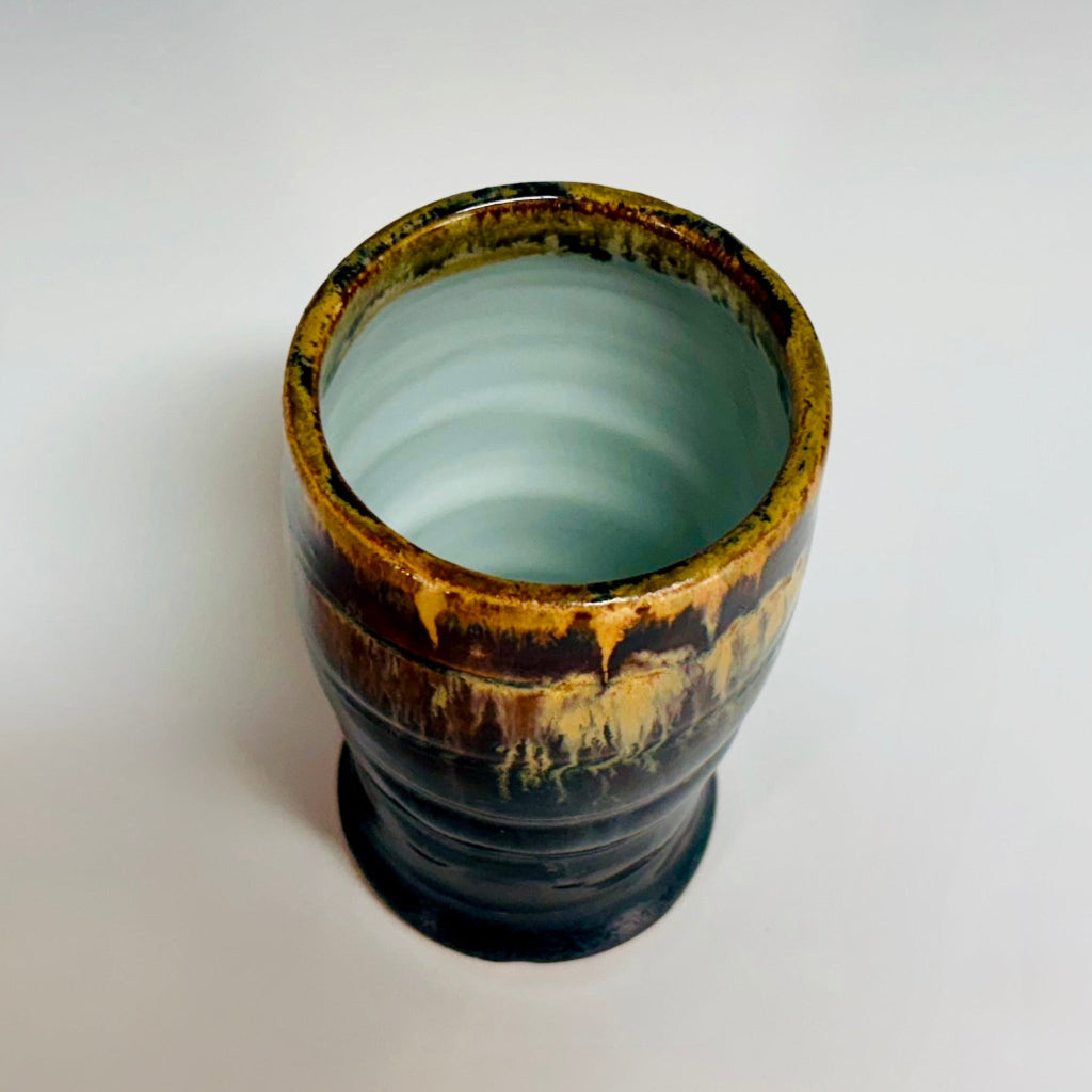 Handcrafted stoneware tumbler with horizontal ridges and blue-black to amber wood-fired glaze effect and a white interior.