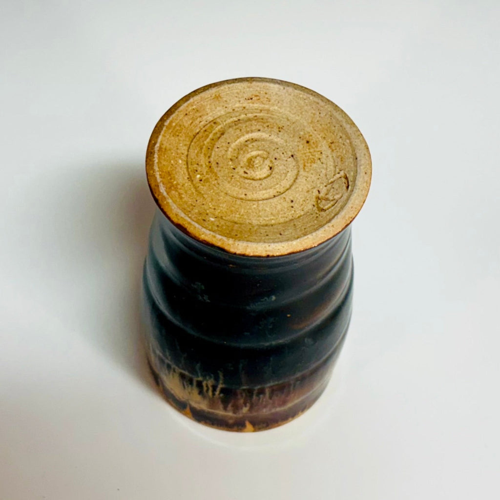 Handcrafted stoneware tumbler with horizontal ridges and blue-black to amber wood-fired glaze effect bottom view with a spiral.