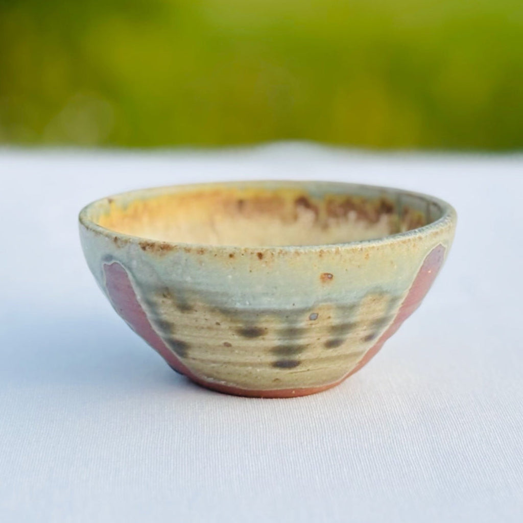Handcrafted pottery ring dish with soft green drips and stripes of amber brown highlighting round bowl shape.