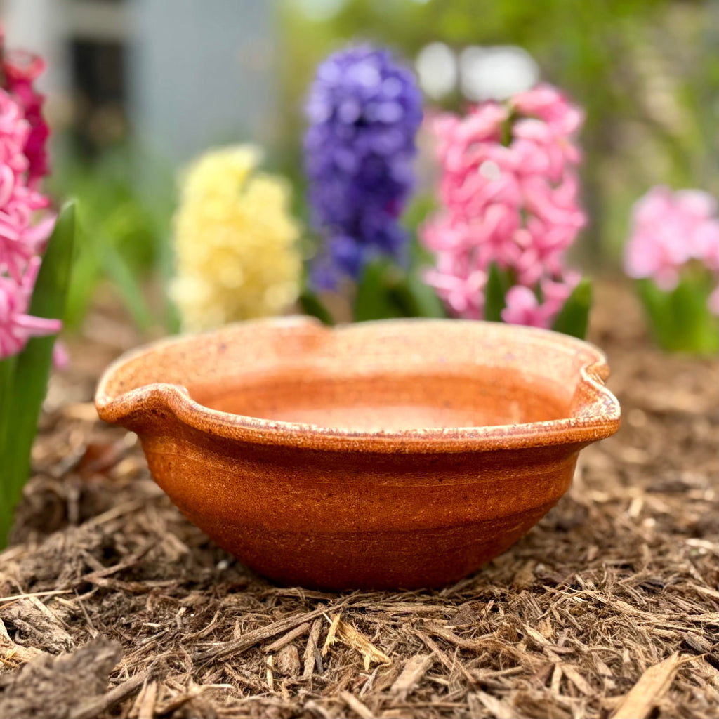 Artisan amber stoneware planter sitting on a patio with pink roses and green grass in the background.