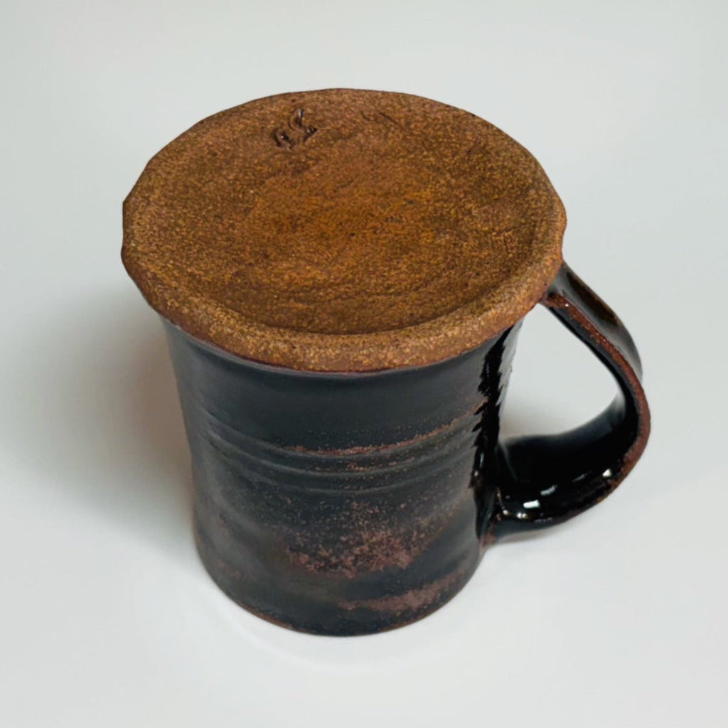 Bottom view. Handcrafted rustic black Tenmoku stoneware mug with brown rim accent and curved handle, wood-fired in Danbury, NC.