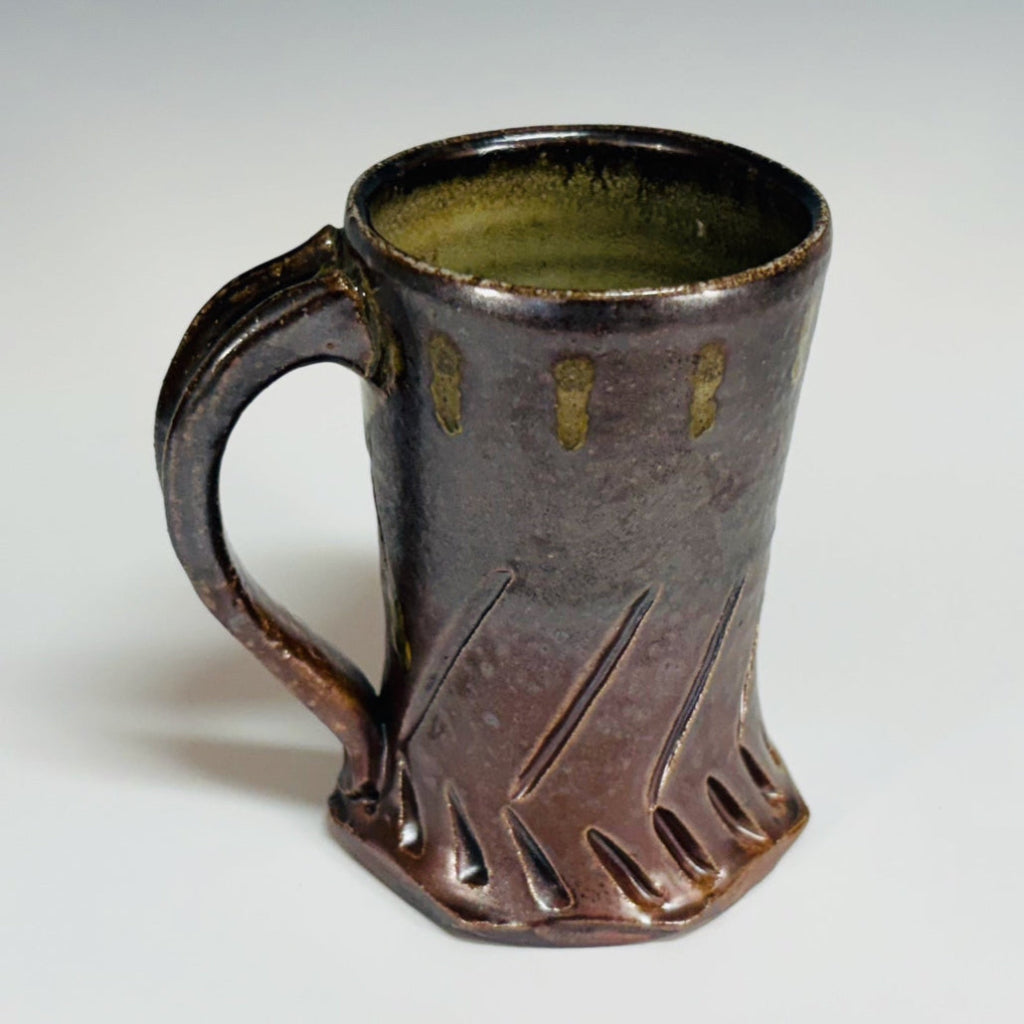 Handcrafted gray stoneware mug with carved chevron pattern, amber glaze drips and curved handle.