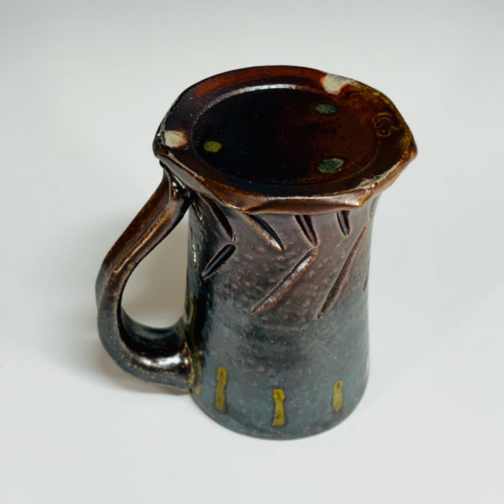 Bottom view. Handcrafted gray stoneware mug with carved chevron pattern, amber glaze drips and curved handle.