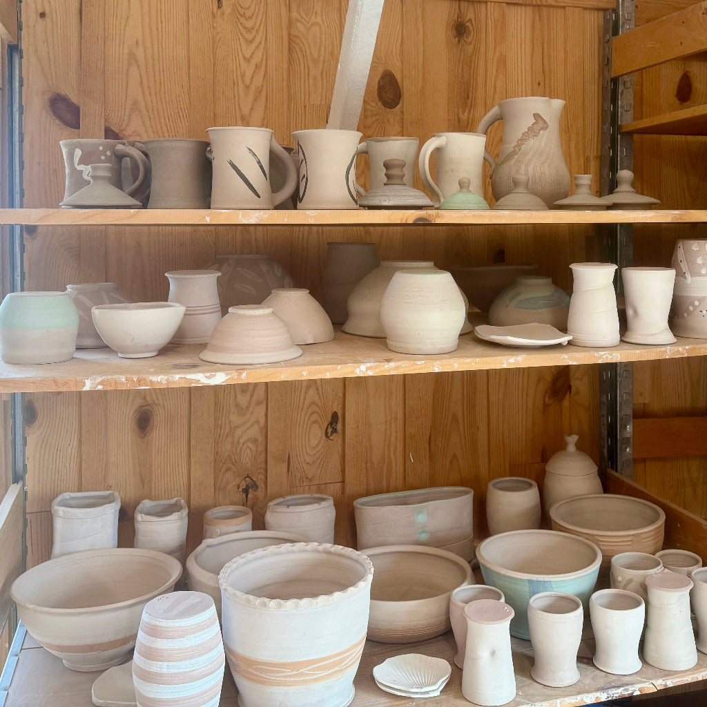 Three shelves of pottery pieces awaiting firing.