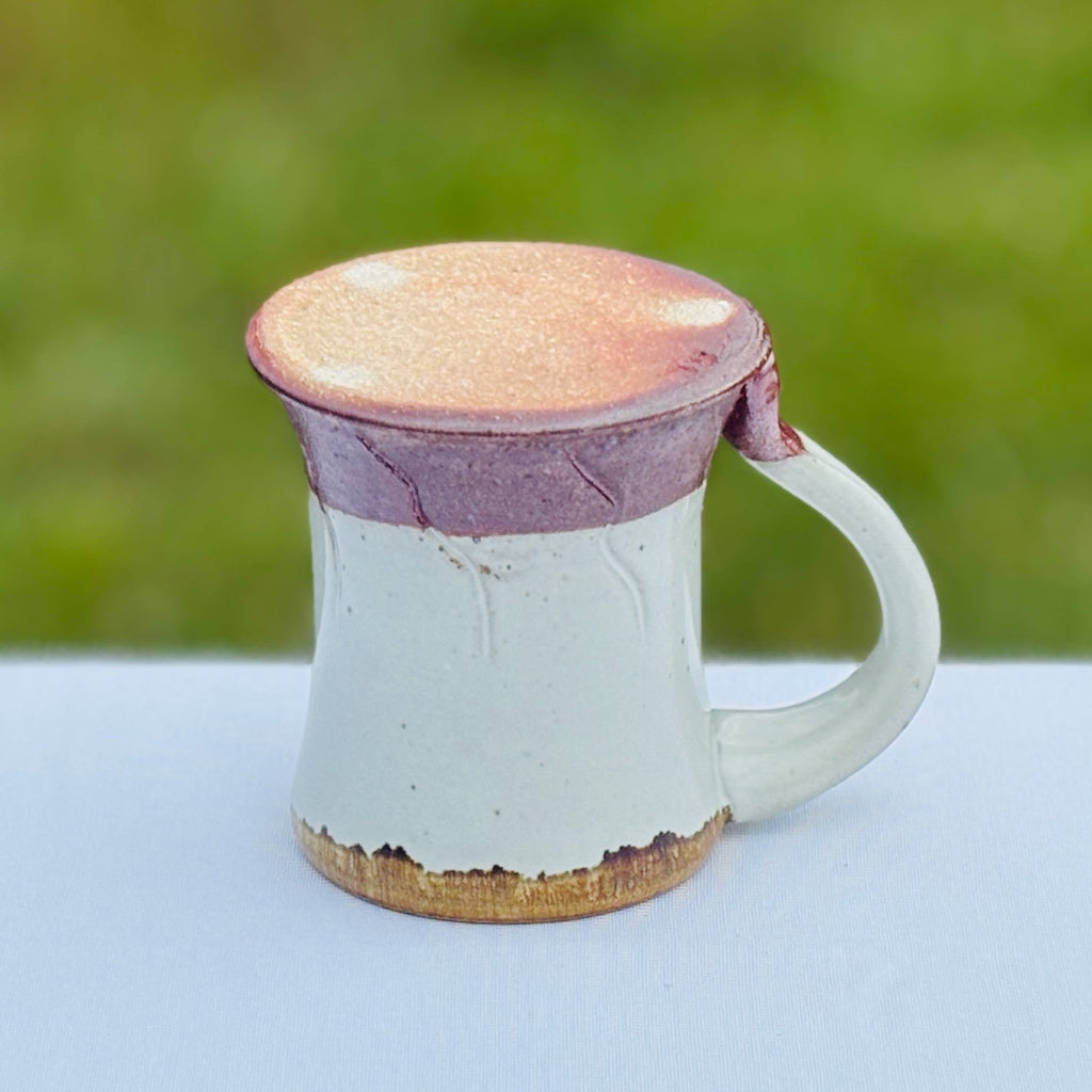 Bottom View: Pottery mug with an unglazed bottom with three white dots and artist's mark, and a gold rim which contrasts nicely with the glossy white glaze and rich brown base. Delicate abstract carved decorations. Made in Danbury, NC. 