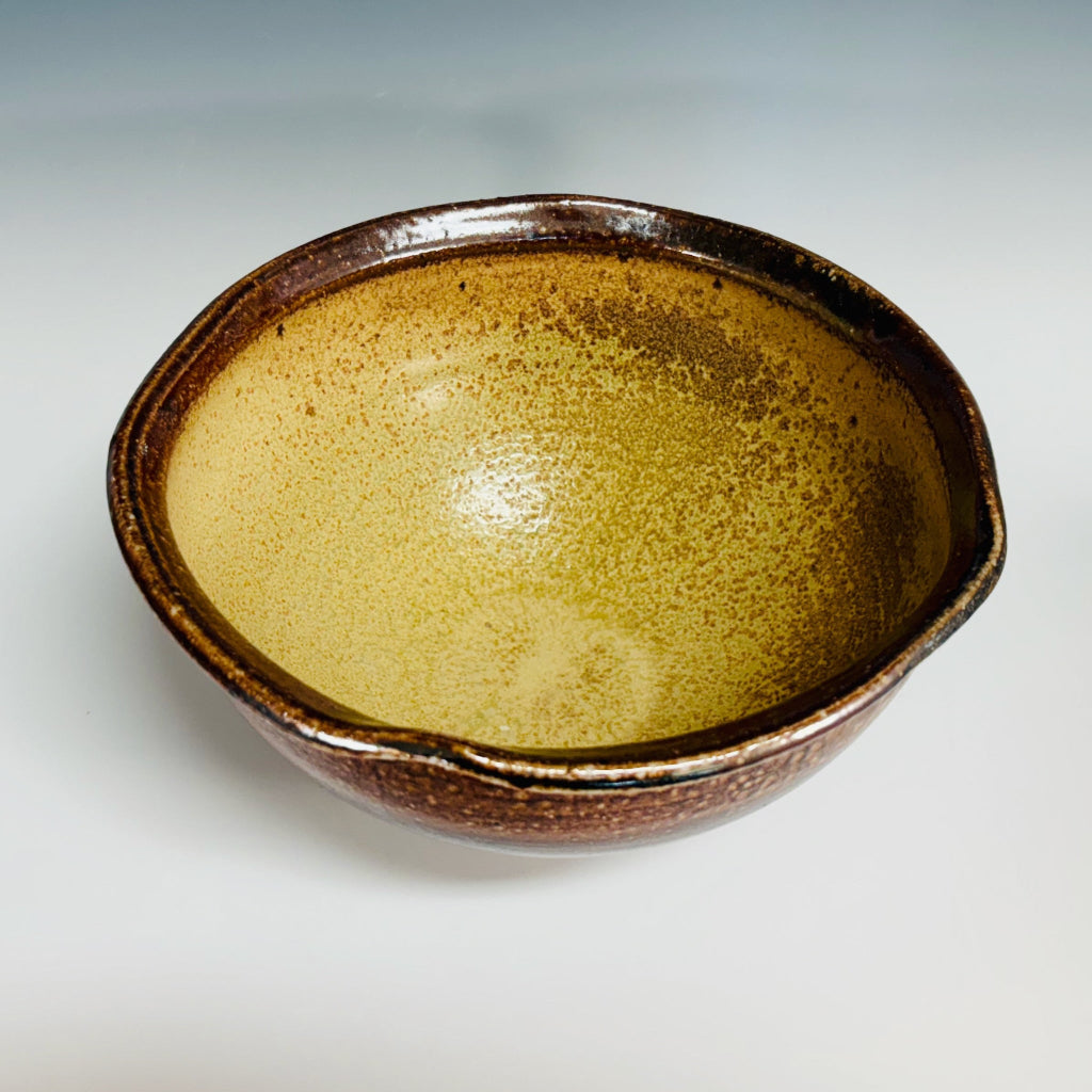 Handcrafted amber and brown speckled stoneware serving bowl with smooth  yellow speckled interior and textured gradient exterior.
