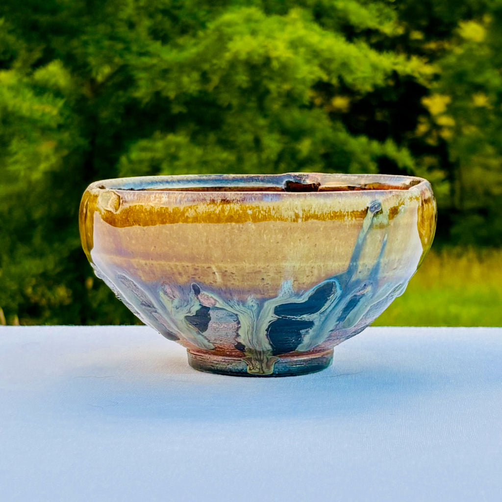 Handmade ceramic bowl with artistic design on a white surface with a green blurred background