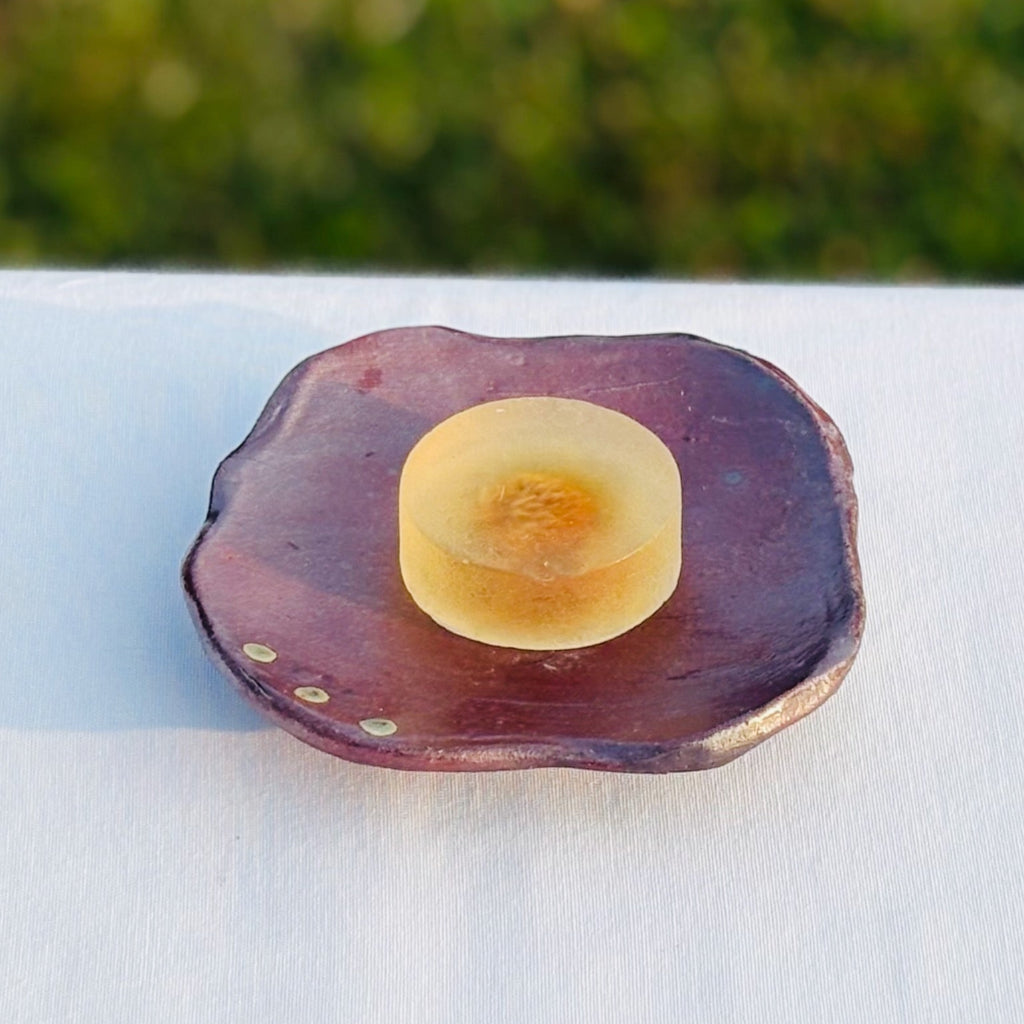 Unglazed ceramic soap dish with natural with blue slip on a neutral surface and yellow glycerin soap