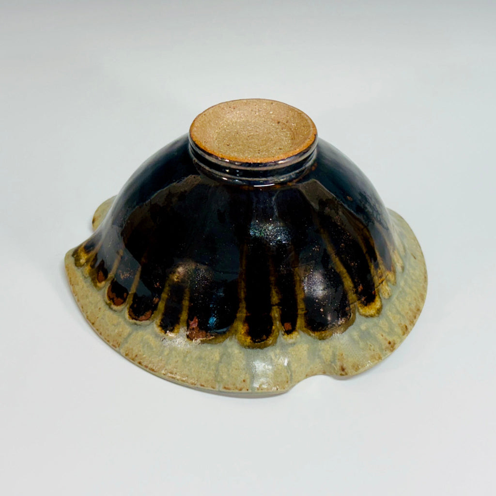 Handcrafted ceramic bowl with an unglazed foot and an asymmetrical wavy rim featuring dramatic black to beige drip glaze finish