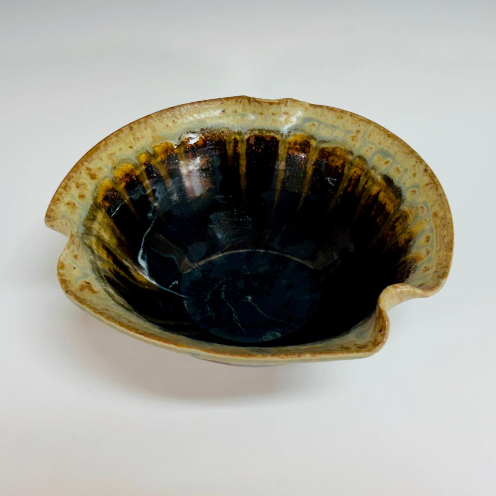 Handcrafted ceramic bowl with asymmetrical wavy rim featuring dramatic black to beige drip glaze finish on a white background