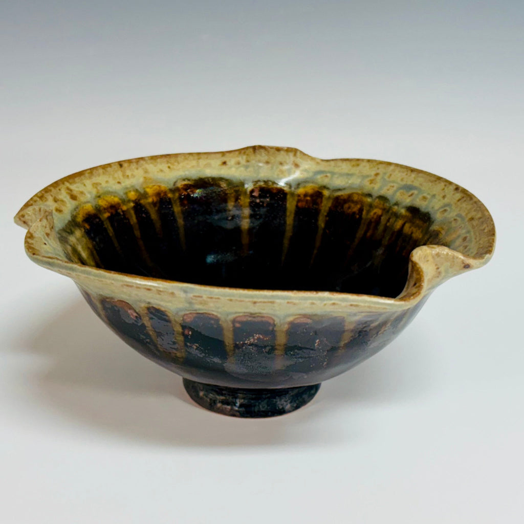 Handcrafted ceramic bowl with asymmetrical wavy rim featuring dramatic black to beige drip glaze finish on a white background