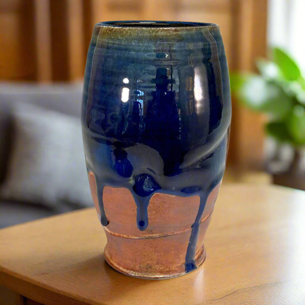 A medium ceramic vase with a deep blue glaze cascading over a natural shino glaze, displayed on a wooden surface.