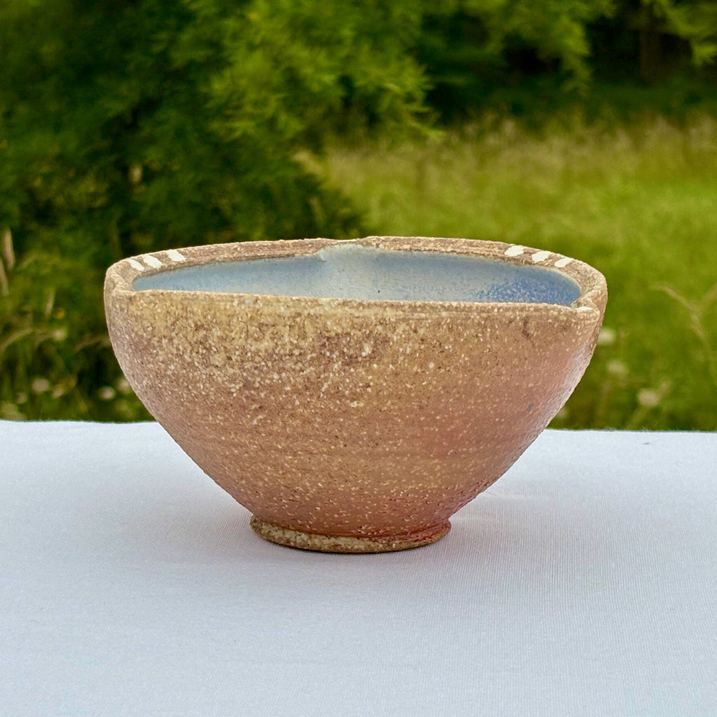 Small porcelain bowl with textured surface and blue interior on a white surface with greenery in the background