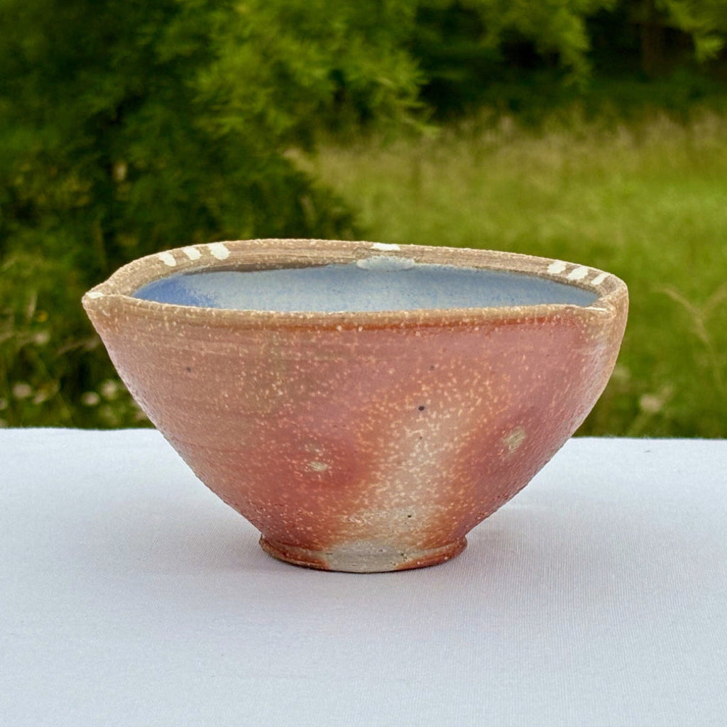 Small porcelain bowl with a blue interior on a white surface with a green outdoor background