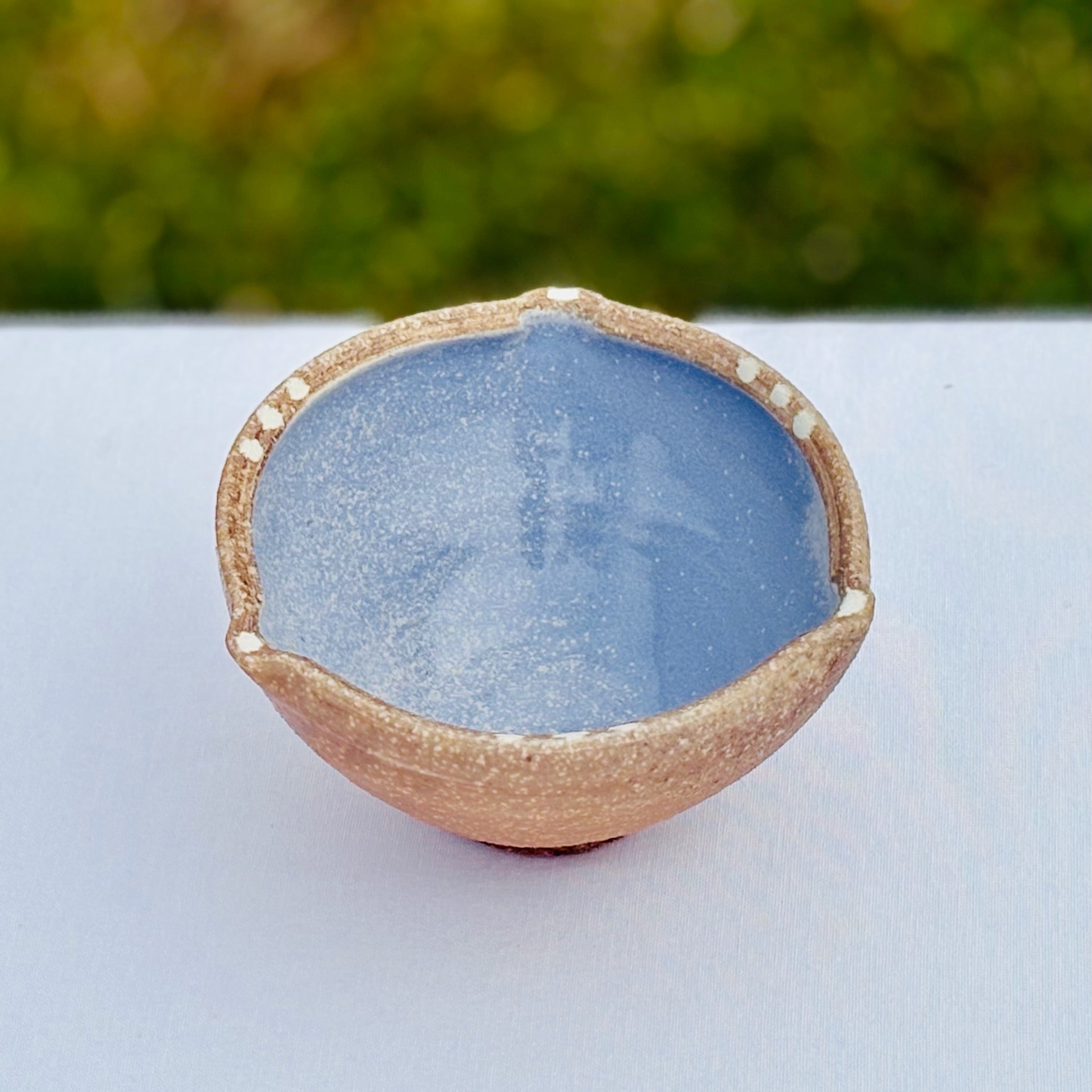handmade porcelain bowl with blue interior and brown exterior on a white surface with blurred green background