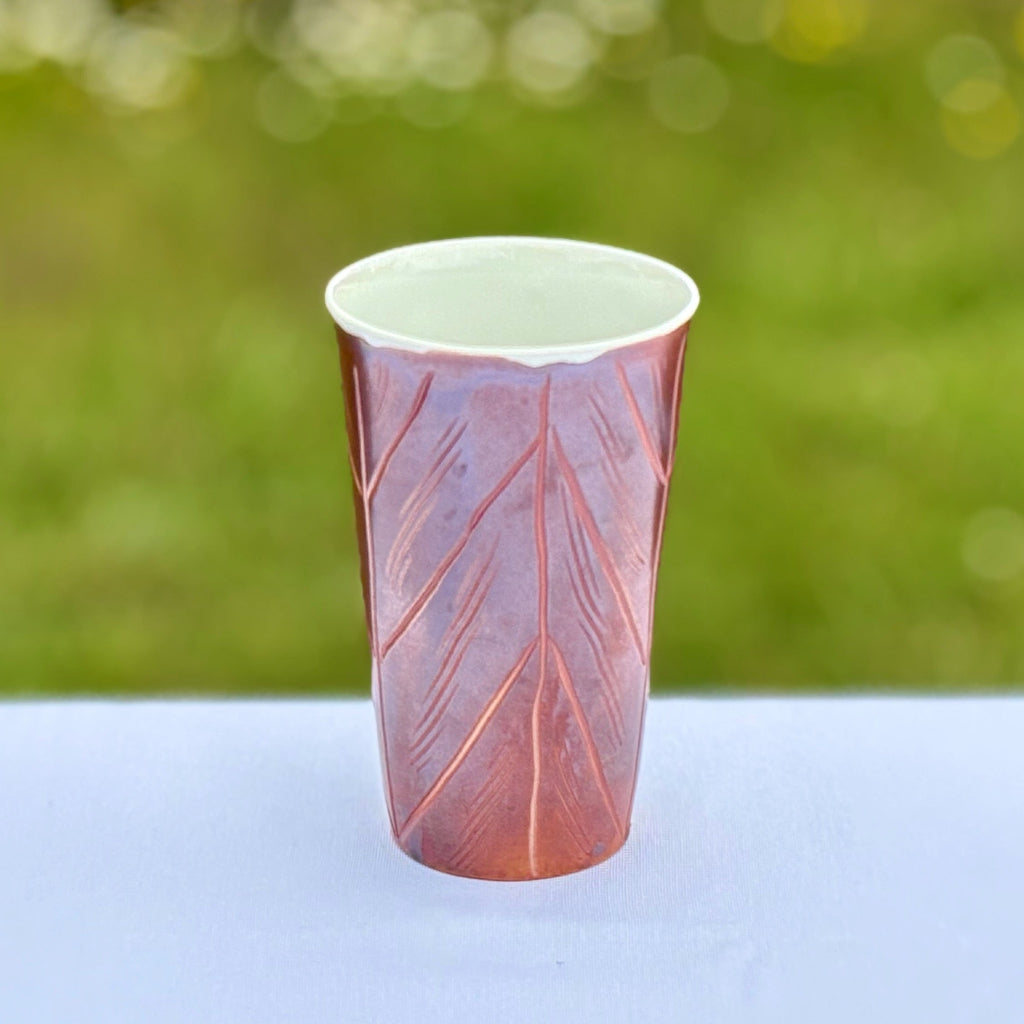 Porcelain cup with white interior and rich red/brown metallic sheen outside and decorative carved lines  