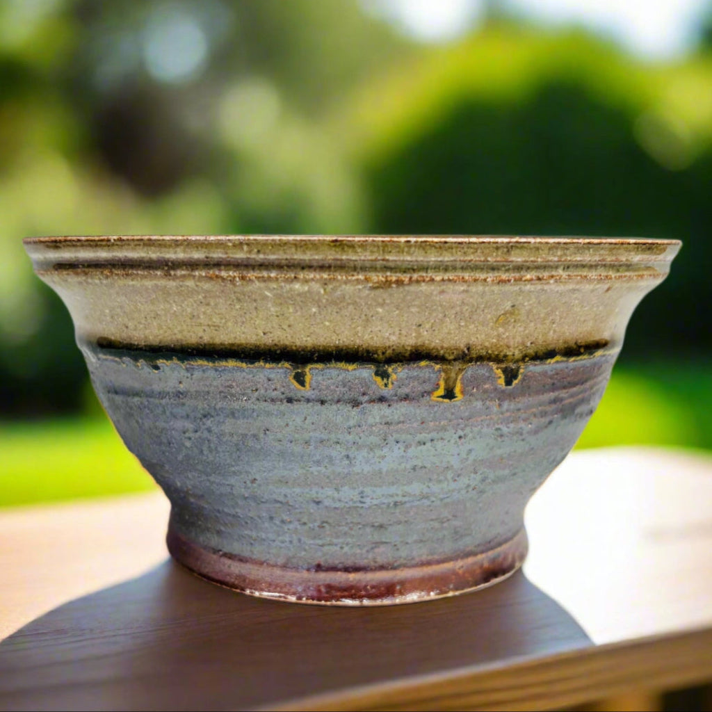 Handcrafted blue-gray and cream ceramic planter with drainage hole, side profile showing textured glaze on table in yard.