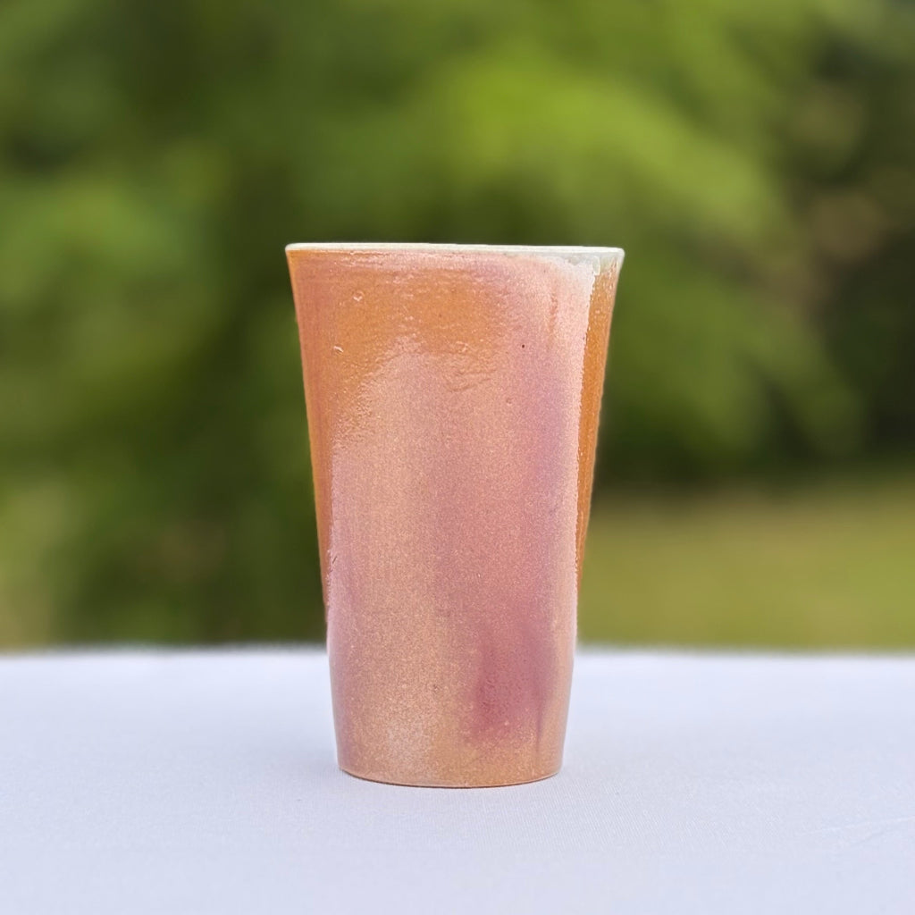 Handcrafted wood-fired porcelain cup with a pink/peach gradient finish, unglazed exterior, and white interior glaze