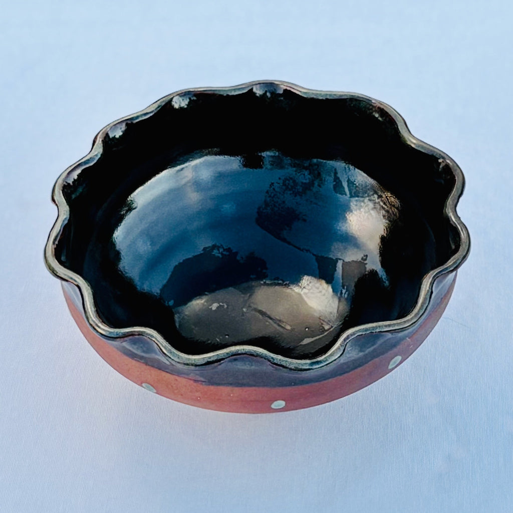 Pottery bowl with a glossy black shino interior and a scalloped rim on a neutral background