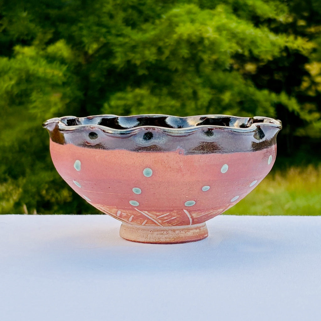 Amber ceramic bowl with scalloped edge on a white surface with greenery in the background