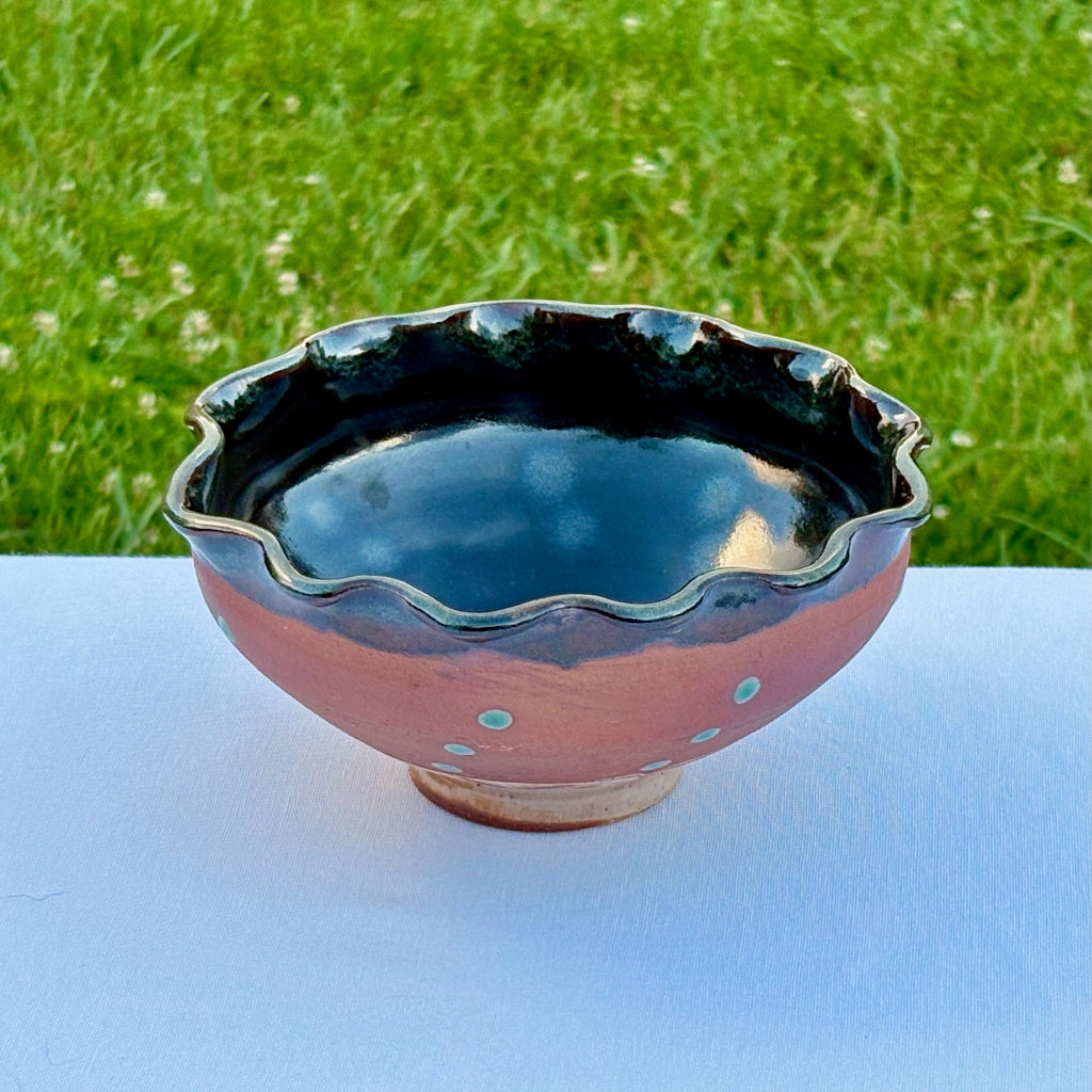 Artisan pottery bowl with a shiny dark brown undulating rim and hand-trailed green slip pattern