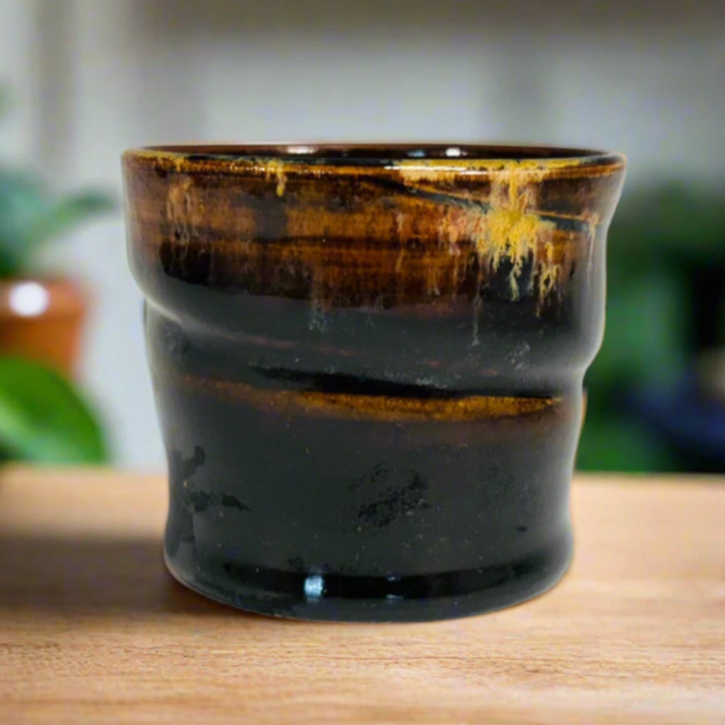 Handcrafted tenmoku ceramic cup with rich black glaze and amber gold drip detail, featuring slight asymmetrical form perfect for tea or sake, artisanal pottery homeware.