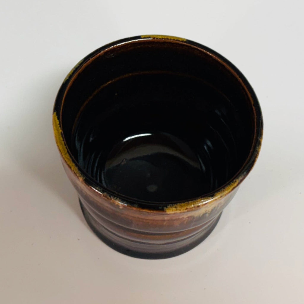 Handcrafted tenmoku ceramic cup with rich black glaze and amber gold drip detail, featuring slight asymmetrical form perfect for tea or sake, artisanal pottery homeware.
