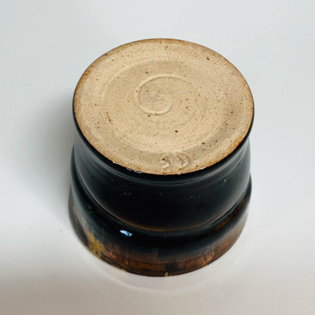 Handcrafted tenmoku ceramic cup with rich black glaze and amber gold drip detail, featuring slight asymmetrical form perfect for tea or sake, artisanal pottery homeware.