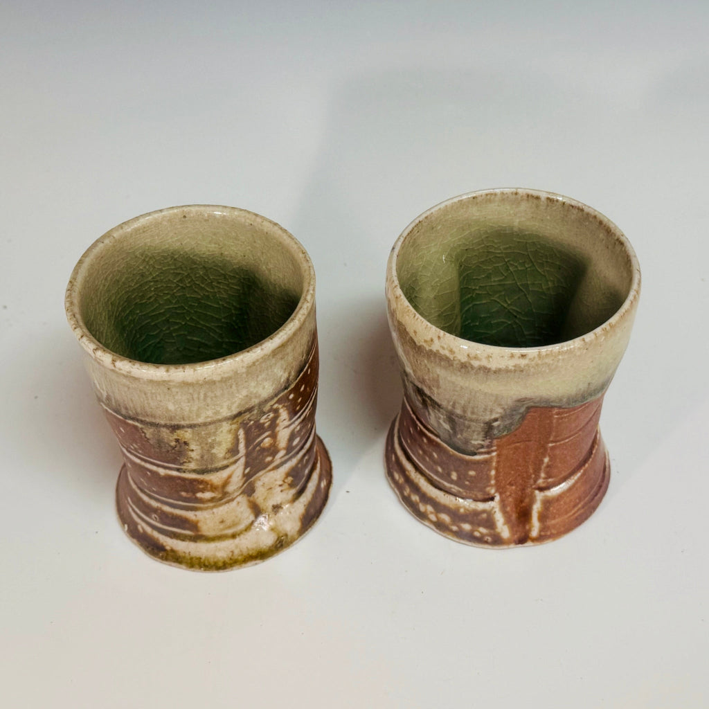 Pair of handcrafted wood-fired ceramic tumblers with creamy interior and rim and warm earth-toned bases with natural ash effects