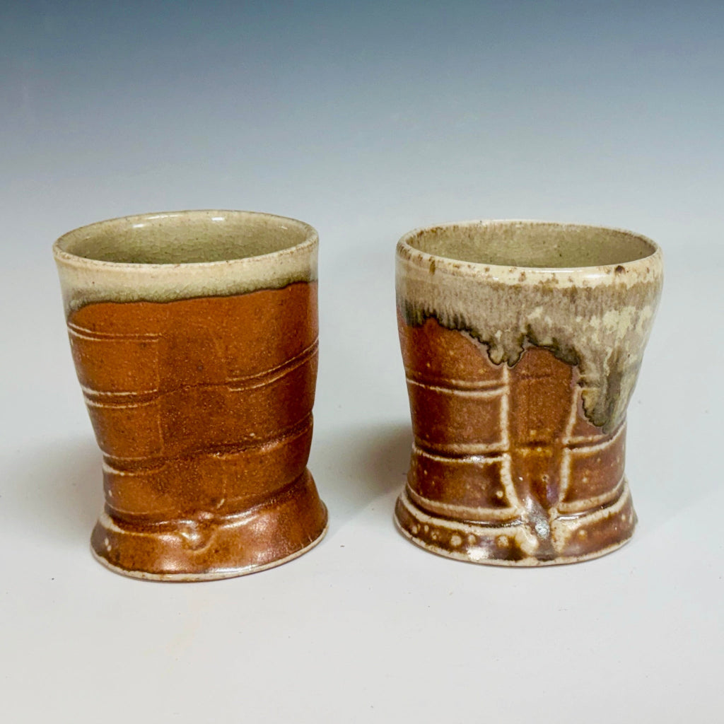 Two ceramic cups with a smooth celadon glaze inside and a vibrant orange flashing slip outside, displayed against a neutral background.
