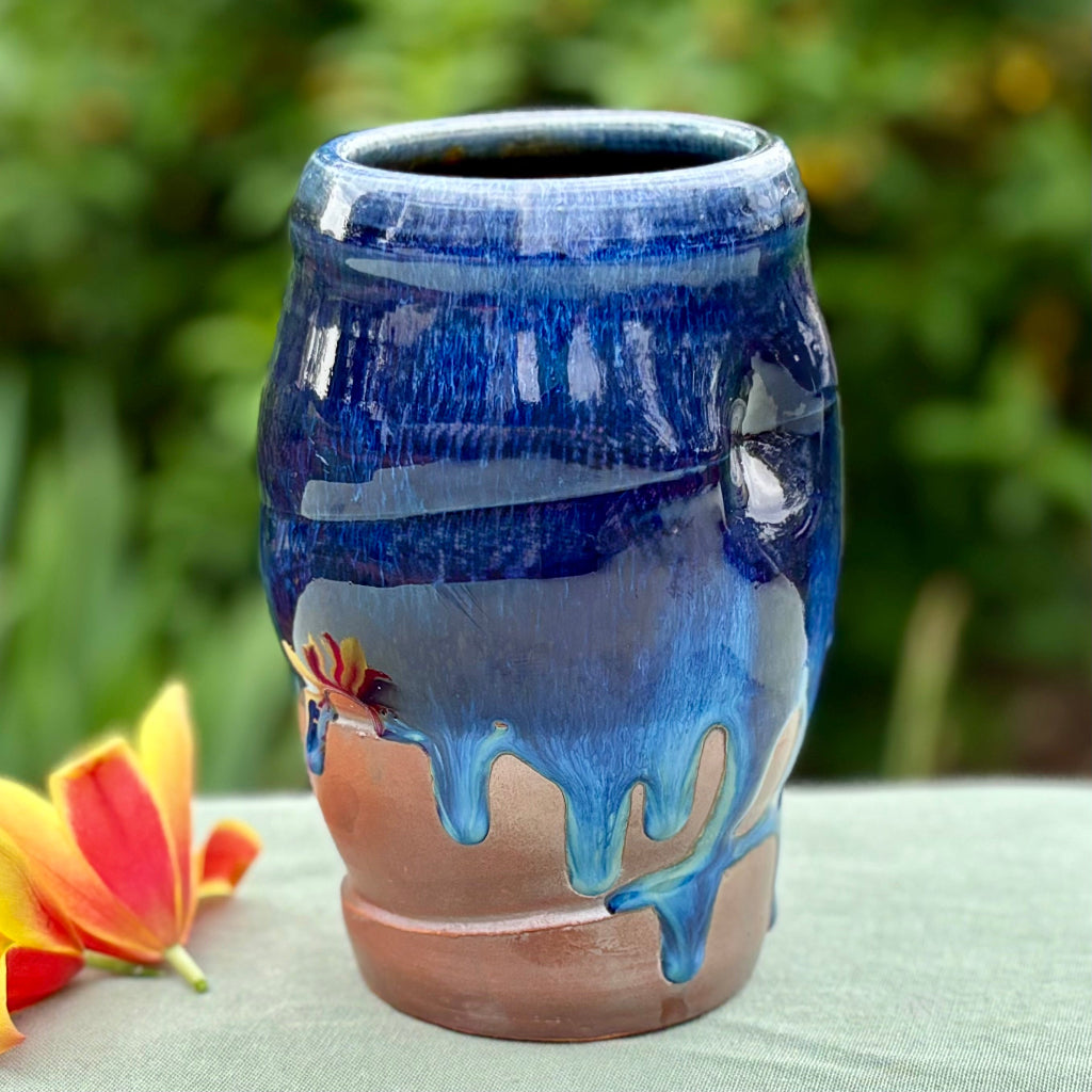 Cobalt glaze ceramic vase with deep blue glaze flowing over orange flashing slip with flower and greenery in background