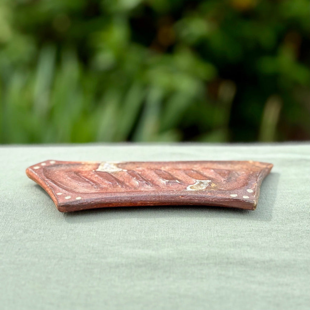 Handmade rectangular soap dish with ridged design and decorative dots in rustic terracotta tones on a a green cloth with greenery in the background