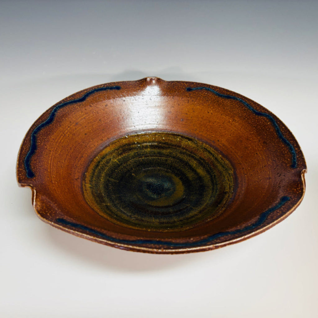 Handcrafted ceramic serving bowl with wavy rippled edge, blue accent lines, and warm brown glaze with golden-green center.